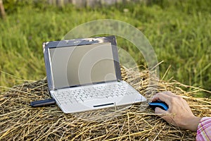 Laptop with modem lies on a haystack near a woman hold her hand