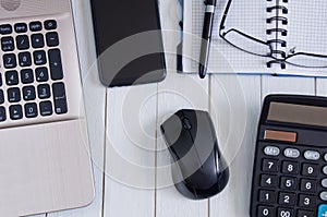 Laptop with mouse, calculator, notebook, pen and smartphone on white wooden table