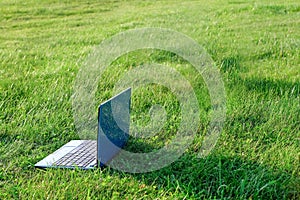 Laptop on natural green grass background. Freelance concept, work and study outside. Copy space