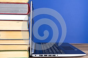 Laptop next to a stack of colorful books on a wooden table on a blue background