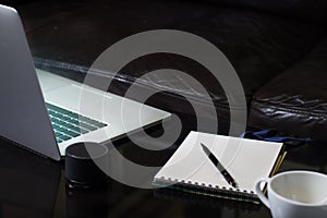 Laptop notebook and coffee cup on mirror table with black sofa