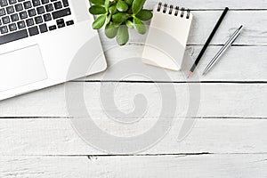 Laptop, notebook, pens and small succulent on white wooden desktop. Business background.