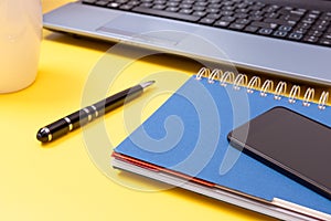 Laptop, notebook, smartphone and pen on yellow background. Office desk table with modern accessories