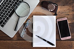 Laptop, Notebook, smartphone, spectacle, camera and magnifying glass on wooden table