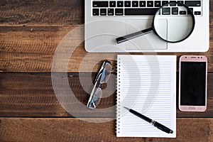 Laptop, Notebook, smartphone, spectacle and magnifying glass on wooden table