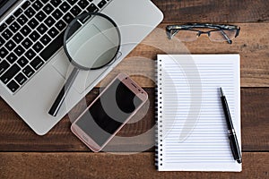 Laptop, Notebook, smartphone, spectacle and magnifying glass on wooden table