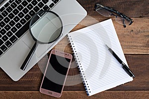 Laptop, Notebook, smartphone, spectacle and magnifying glass on wooden table