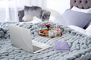 Laptop, notebook and tray with breakfast on bed in stylish room