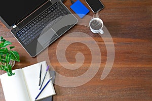 Laptop with office supplies, green plant and hot black coffee with smoke on vintage grunge wooden desk background