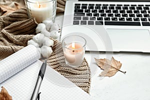 Laptop, open notebook and burning candles on white wooden table