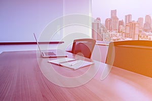 Laptop and pen on notepad for agenda kept on table in empty corporate conference room with cityscape view on background.