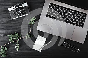 Laptop, photo camera, eyeglasses, rose branch and cup of coffee with white sheet on wooden table