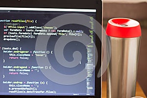 Laptop with programming web code and red capped flask aside