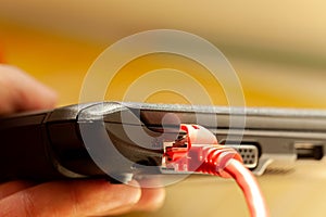 Laptop red network cable connected, netbook internet connection port closeup, detail, copy space. Thin notebook with rj45 plug