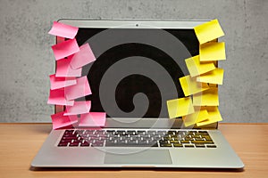 Laptop in reminders with yellow and red stickers notes on the display frame on table with gray wall