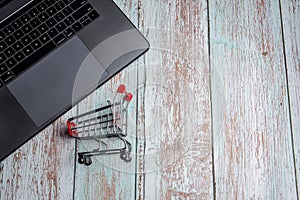 Laptop and shopping cart on wooden table. Online Shopping Concept