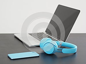 Laptop with smartphone and blue wireless headphones on wooden desk.