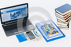 Laptop, smartphone, stack of books, notebook and pens on white wooden table, education office concept background