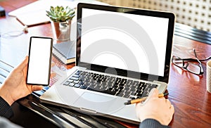 Laptop and smartphone with white blank screens, office interior background