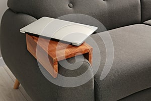 Laptop on sofa with wooden armrest table in room. Interior element