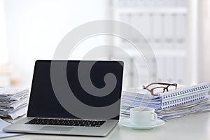 Laptop with stack of folders on table on white background