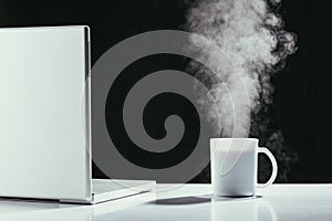 Laptop with steaming cup of tea on table