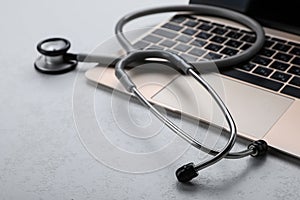 Laptop with stethoscope on white table, closeup. Space for text