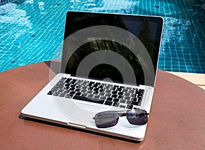 Laptop with sunglasses near the pool