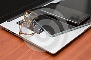 Laptop, tablet, smartphone, eyeglasses on wood table.  Many electronic devices of business people on the desk for work from home