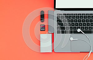 Laptop with USB Type-C adapter, flash drives, headphones and Power Bank on a red background, top view, workplace