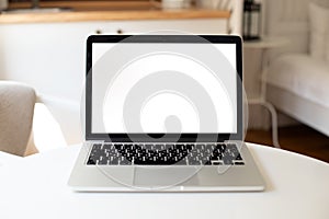 a laptop with a white blank screen stands on table in the interior of the apartment. mockup for