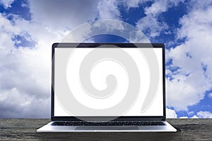 Laptop with white blank screen on wooden table and blue sky back