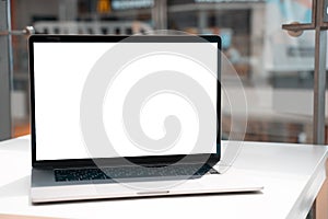 Laptop with white screen in business office or shopping mall. Empty copy space, blank screen mockup. Soft focus laptop