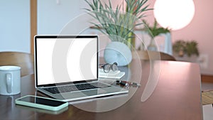 Laptop with white screen, smart phone and glasses on wooden office desk.