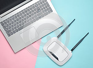 A laptop and a wi-fi router on a colored paper background. Keyboard, touchpad. Modern digital technologies. Copy space. Top view