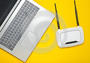 A laptop and a wi-fi router on a yellow paper background. Keyboard, touchpad. Modern digital technologies. Copy space. Top view