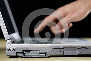 A laptop on a wooden table as seen from a profile with a hand. C