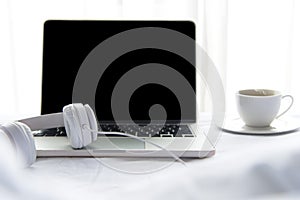 The laptop working and listen music on the white bed and coffee in the sunny day morning holiday. Music and Lifestyle Concept