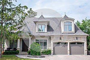 A large 2 story bungalow residential home with grey and brown stucco, brick and stone exterior.