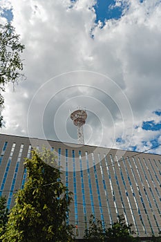 A large 5 ji tower rises above the building in which the sky is reflected