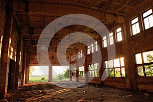 A large abandoned industrial building is lit by light from the windows. Large red brick building