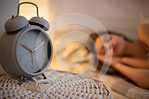 A large alarm clock stands on the cabinet next to the sleeping young woman.