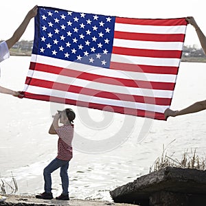 large American flag, child stands under it and looks into the distance through binoculars