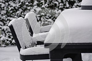Large amount of snow covered chairs and table in a garden
