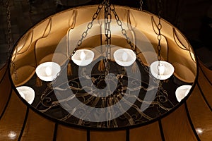 A large antique vintage round metal chandelier of bronze color with decorative elements hangs on the ceiling of a golden