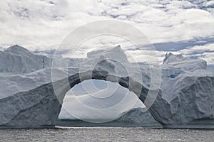 Large through-arch in an iceberg on a cloudy