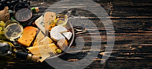 A large assortment of cheeses, brie cheese, gorgonzola, blue cheese, grapes, honey, nuts, red and white wine, on a wooden table.