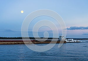 Large barge pushed down Mississippi river at dusk