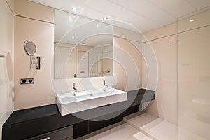 Large bathroom with two ceramic white washbasins on massive black marble countertop along wall and square mirror on wall