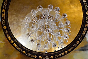 Large beautiful luxurious crystal glass chandelier with pendants and ornaments and a frame of gold ornaments on the high stone cei